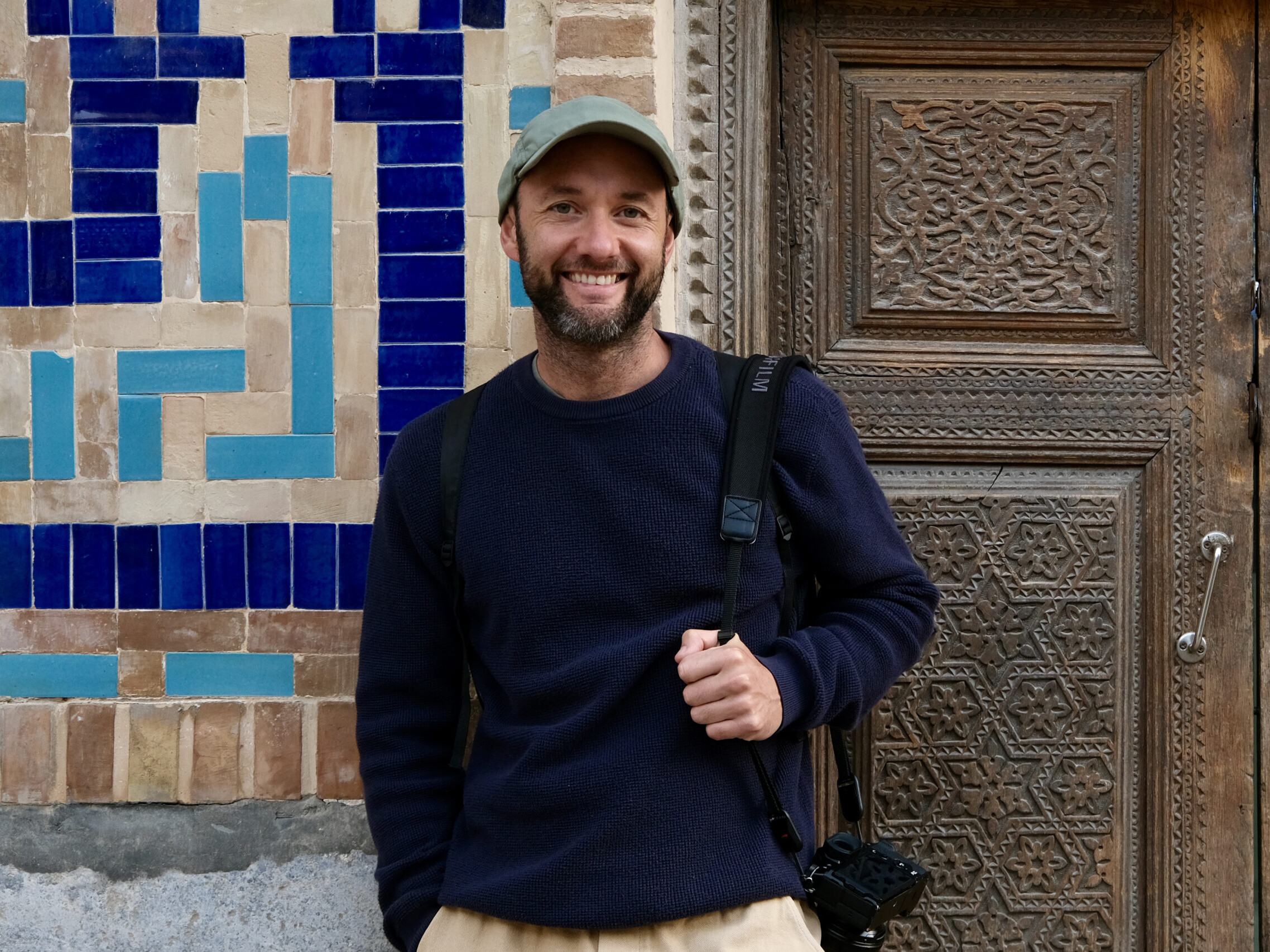 Portrait of travel photographer Lorenz Berna, against a mosaic wall and carved wooden door