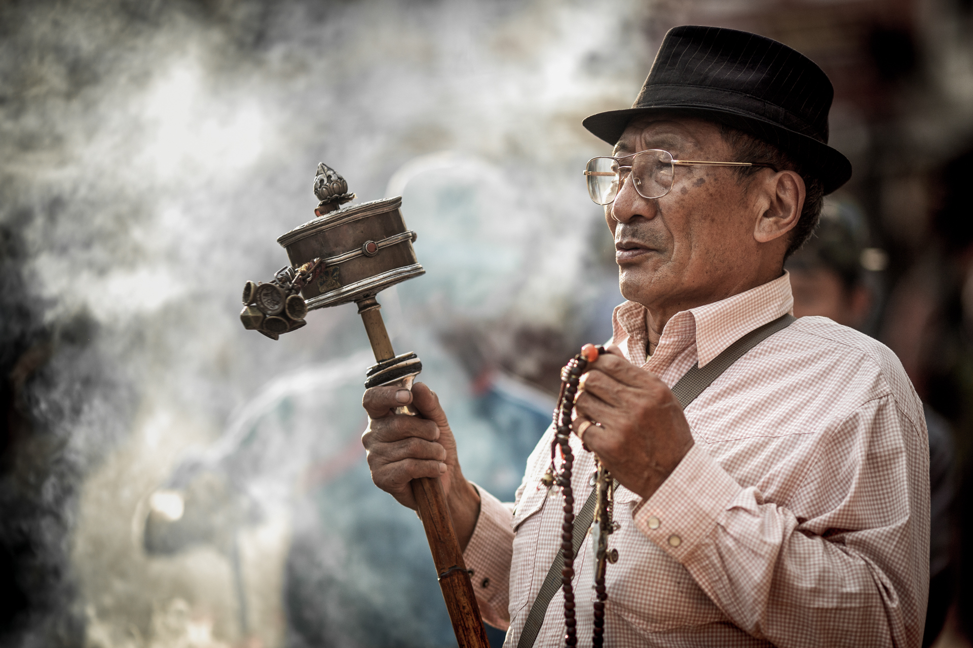 A tibetan man is using a small hand wheel prayer while repeating a buddhist mantra. Nepal photography by Lorenz Berna