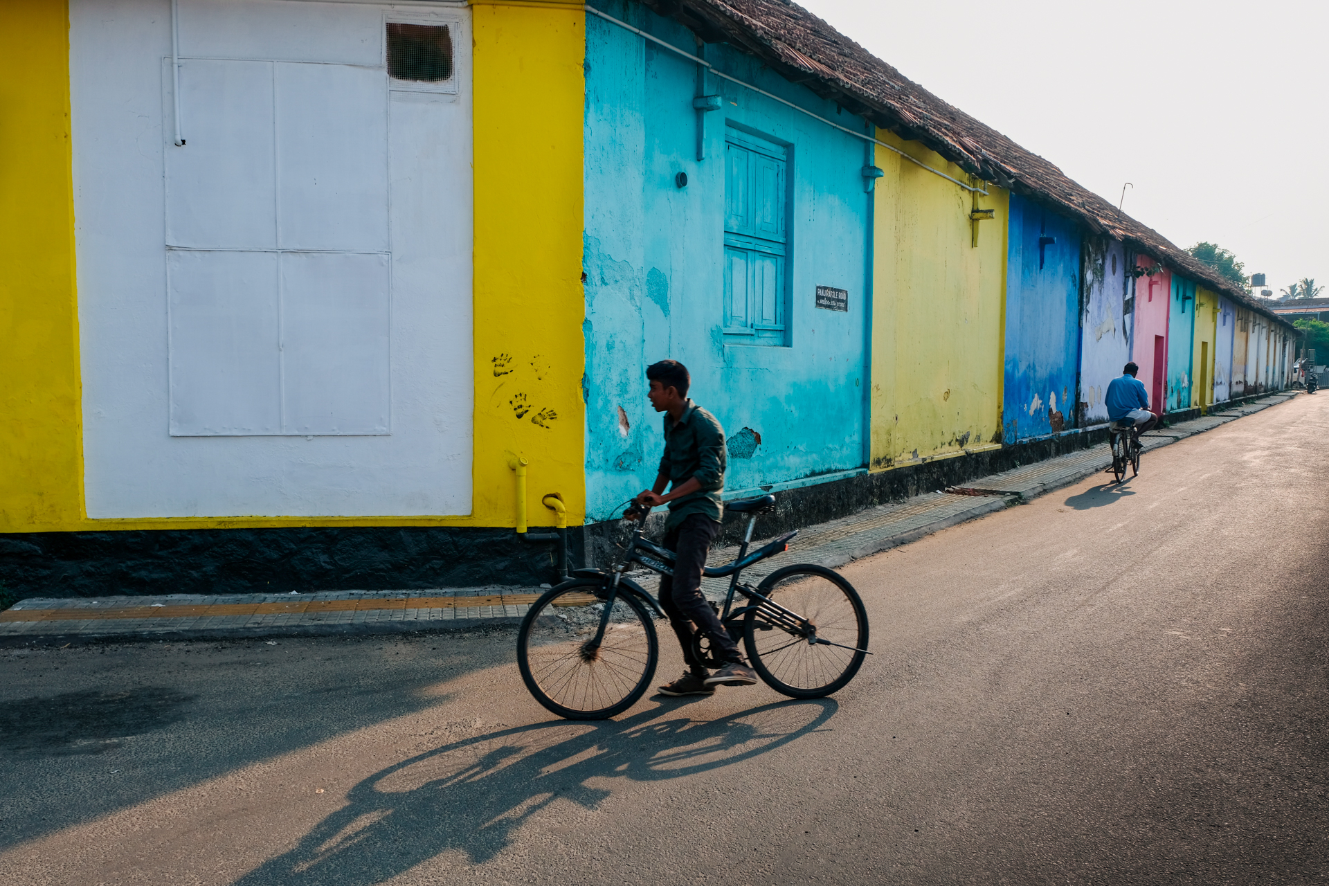 Young man riding a bicycle along a colorful street lined with painted buildings in Fort Kochi