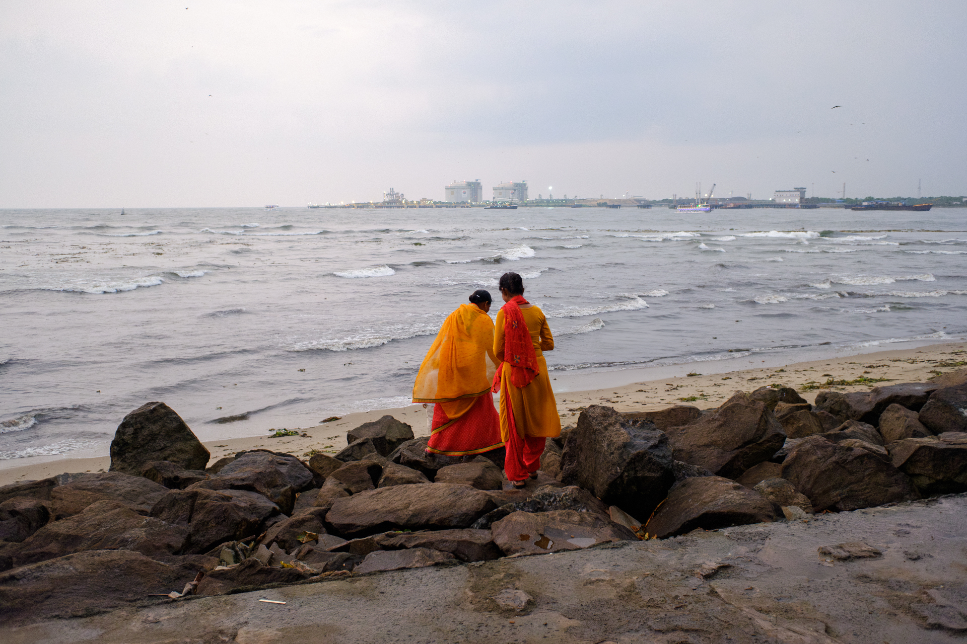 Two women in traditional bright sarees walking along the beach at Fort Kochi, Kerala