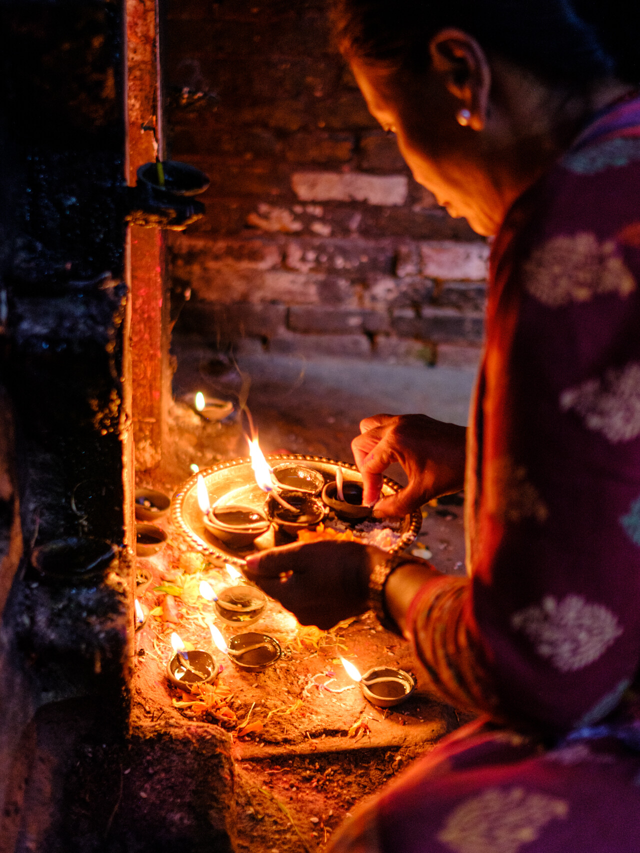 Woman lighting candles in a wood and bricks temples in Bhaktapur, Kathmandu. Nepal Photography by Lorenz Berna