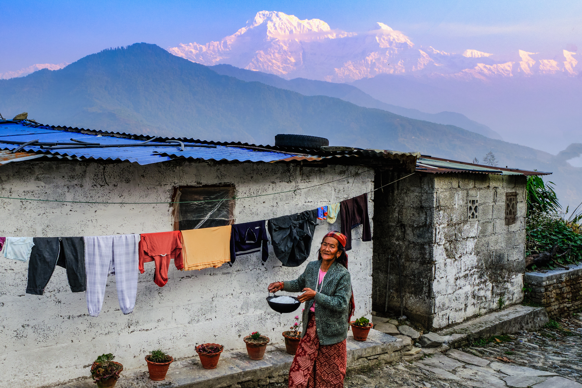 A nepali woman is photographed in front of her house, with the Himalayan range in the background. Extract of the Nepal Photo Tour by Lorenz Berna
