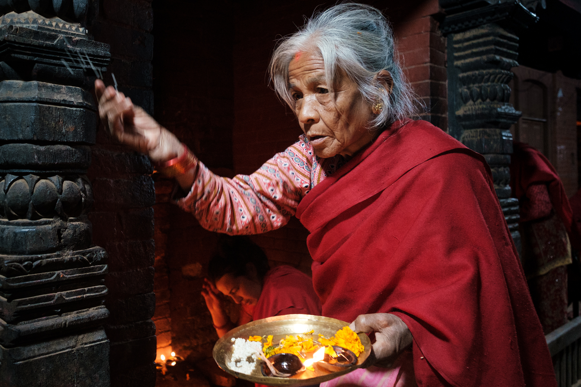 Elderly woman holding a plate of offerings and praying during Laxmi Puja in Nepal