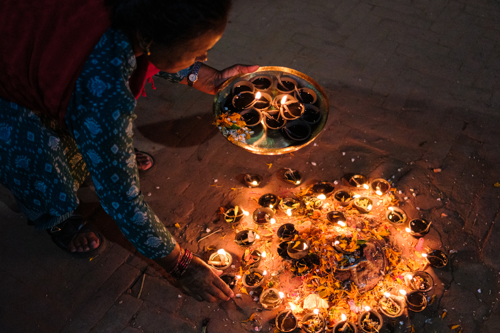 Close-up of a woman placing an oil lamp on the ground mandala during Tihar evening in Nepal