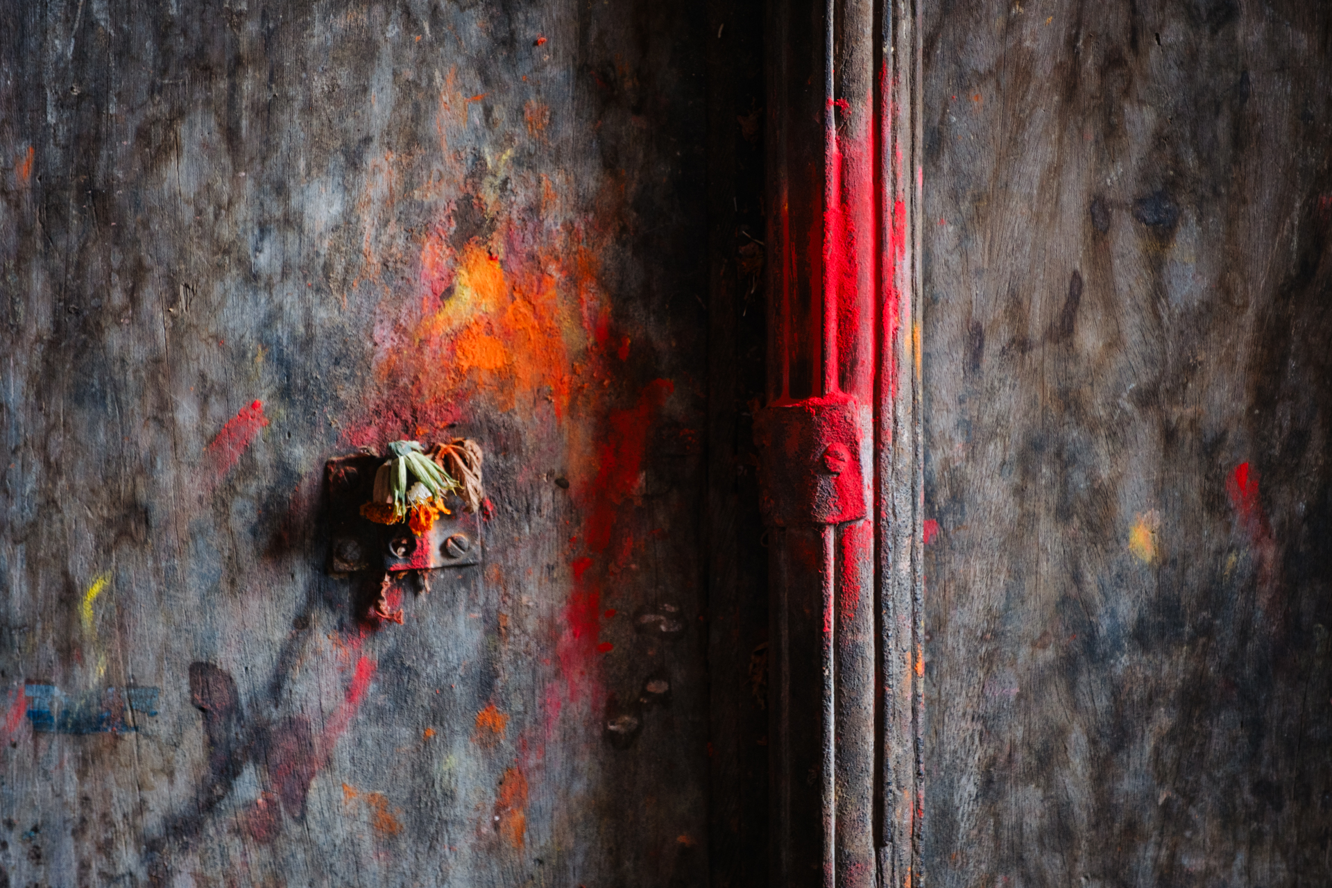 Traditional Nepali wooden door with red and orange powder and dried flower offerings.