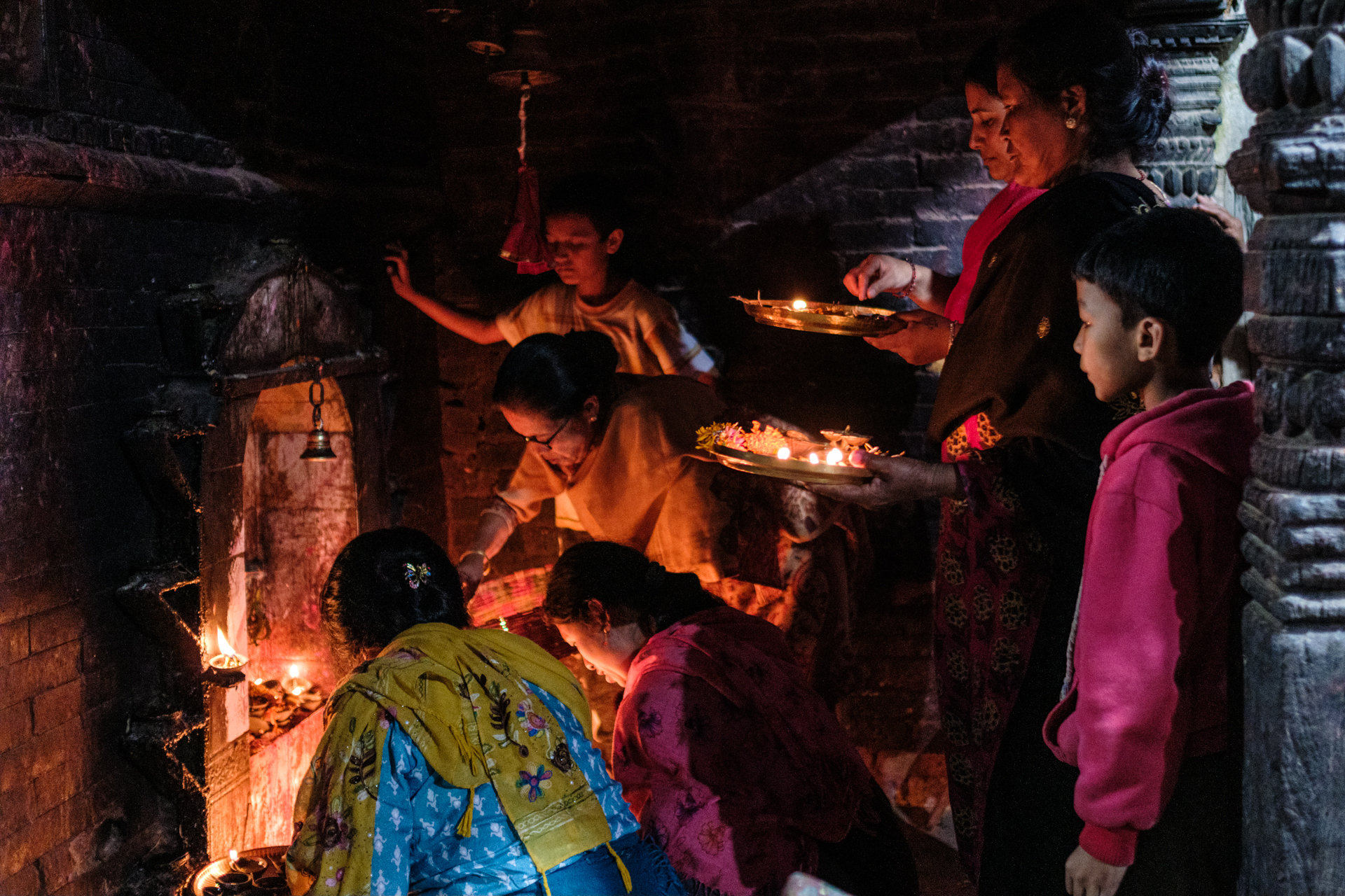 Group of women and children gathered inside a dark temple lighting lamps during Tihar in Nepal