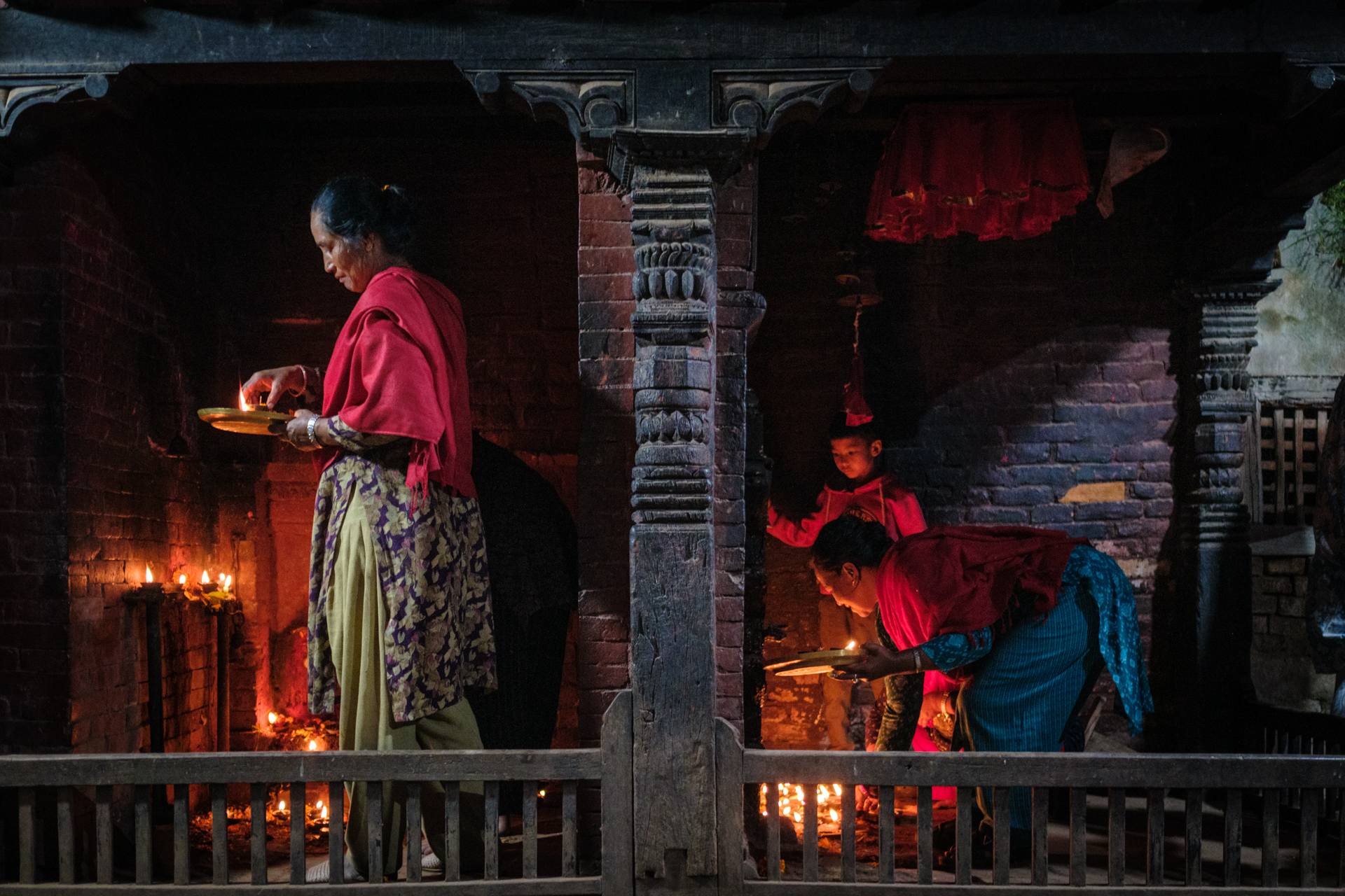 Women lighting oil lamps inside a traditional brick temple during Tihar in Nepal