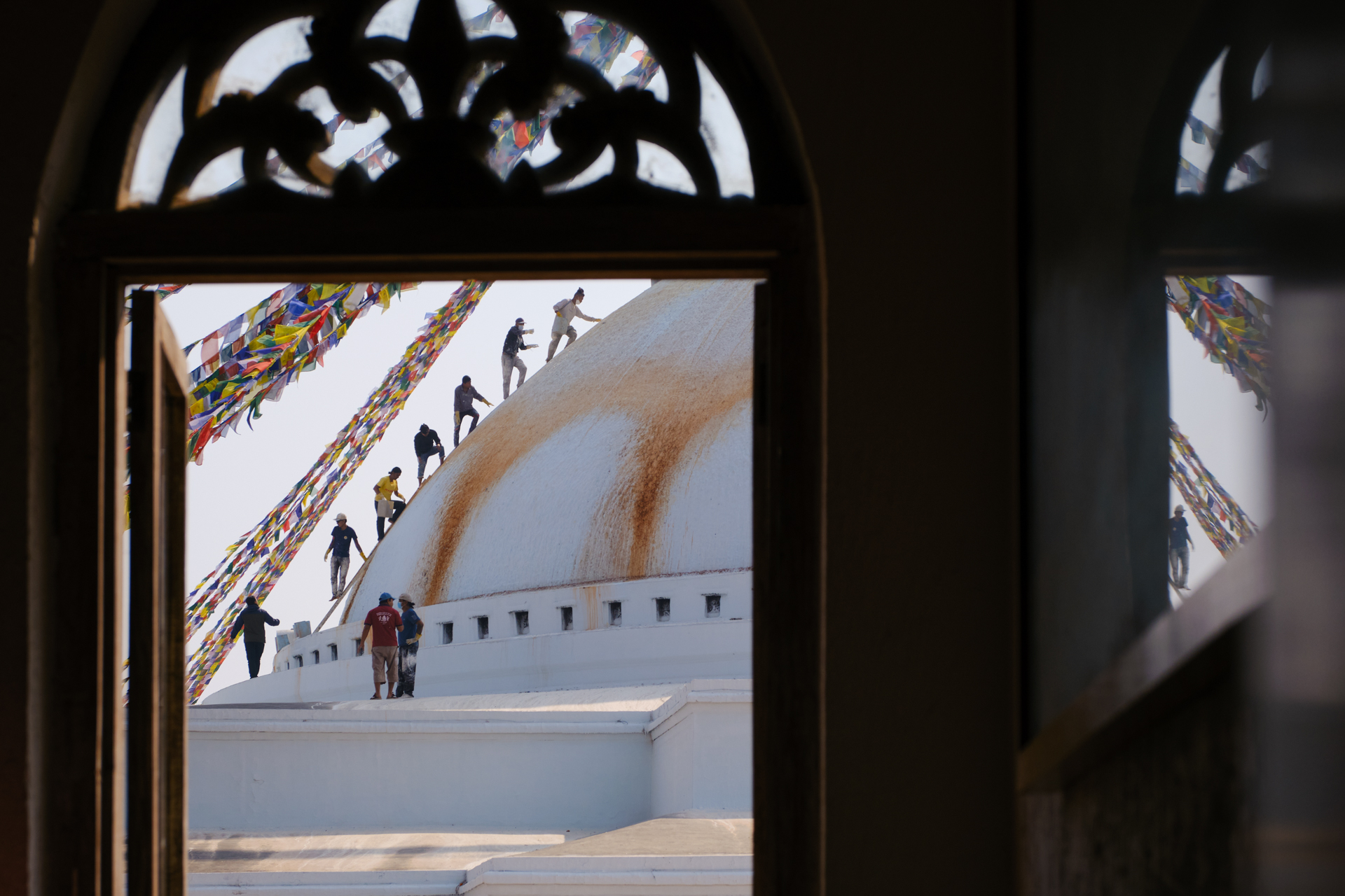 Workers lined up on the sacred Boudhanath Stupa in Kathmandu, captured from the inside of a front window, by travel photographer Lorenz Berna