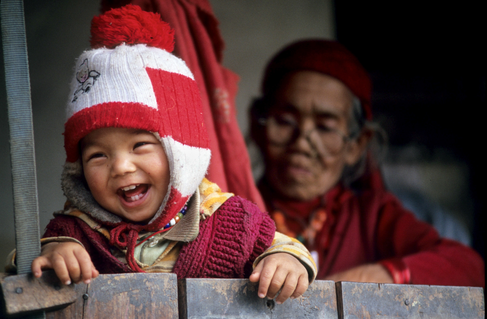 Laughing child in a wool hat during winter in Dhampus – candid portrait from Nepal travel photography