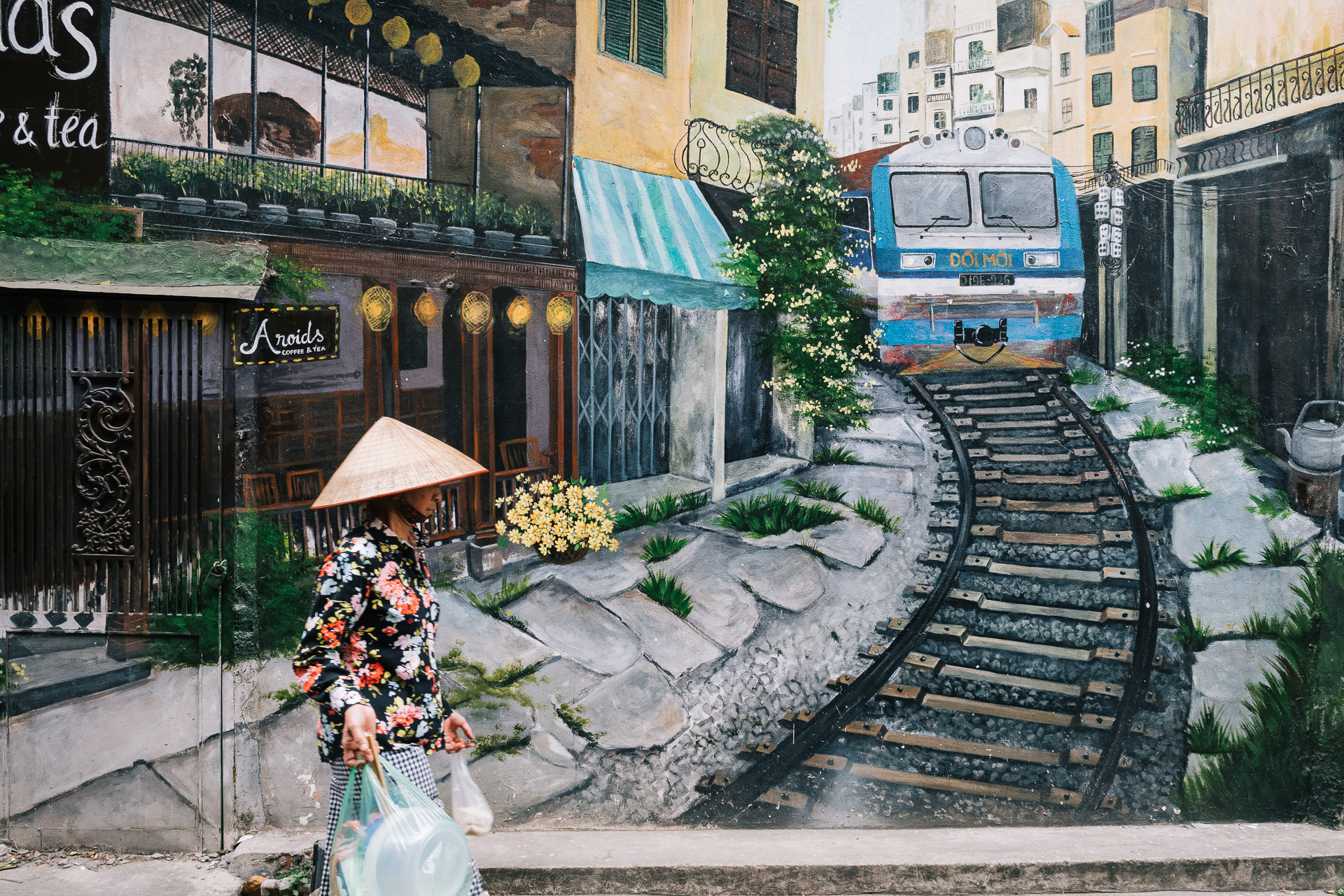 hanoi street photography - A mural depicting Hanoi’s famous train street with a woman in a conical hat passing in the foreground.
