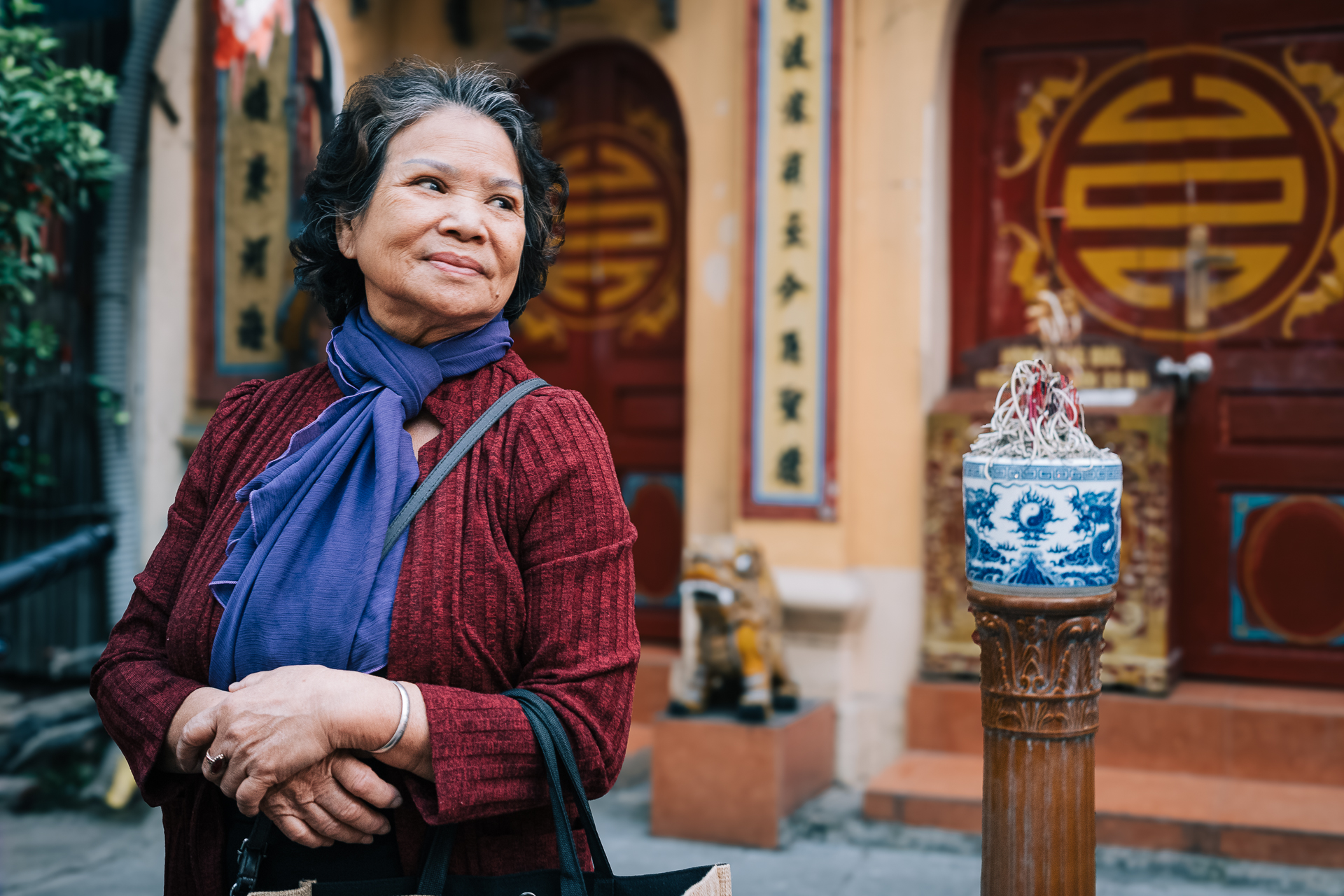 Smiling elderly woman standing outside a traditional temple in Hanoi’s Old Quarter.