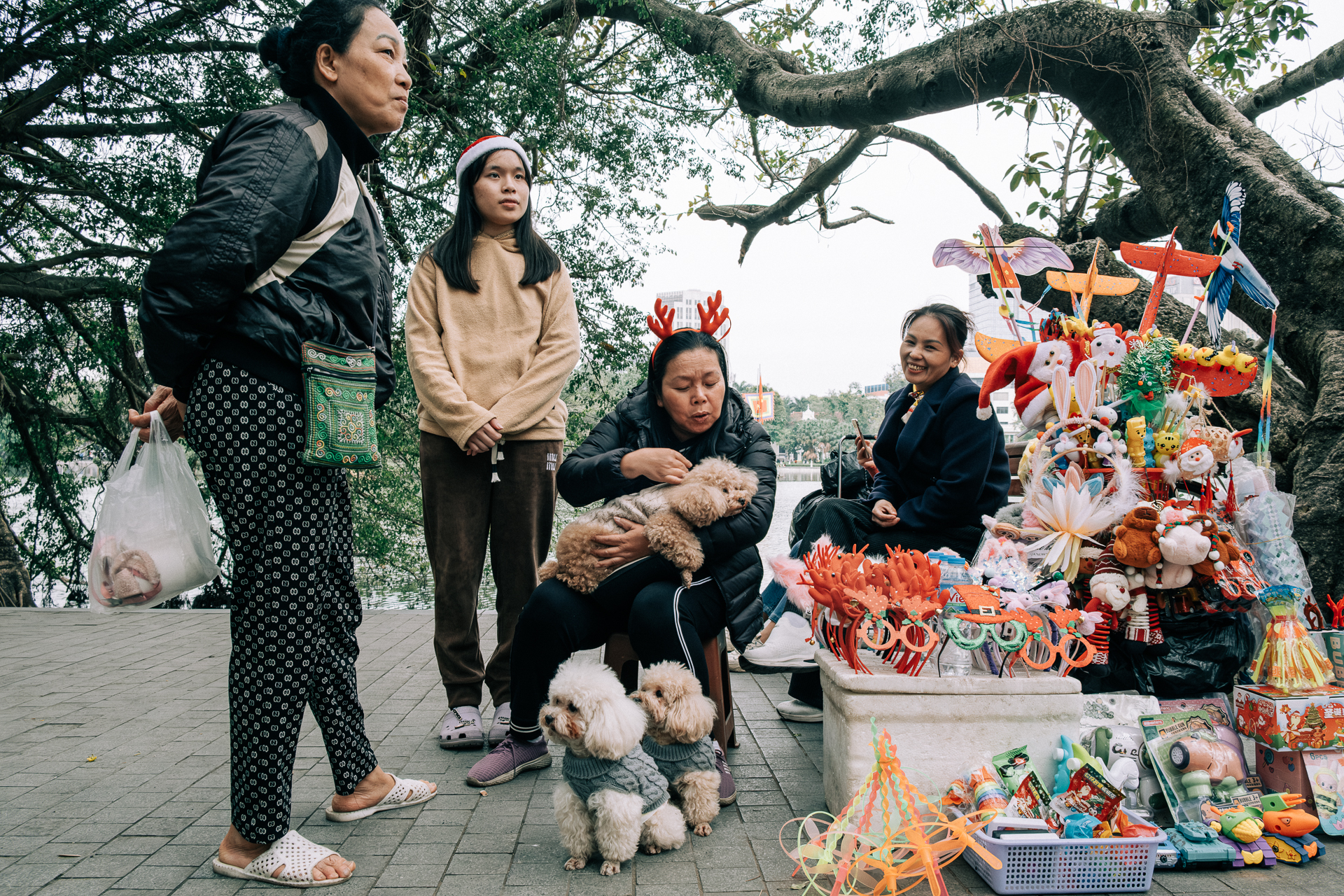 Local women and children sitting beside a street vendor selling Christmas decorations and toys in central Hanoi.