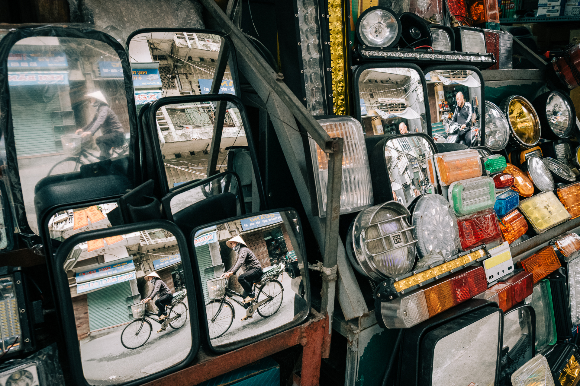 Bicyclists reflected in multiple rearview mirrors at a motorbike repair shop in Hanoi.