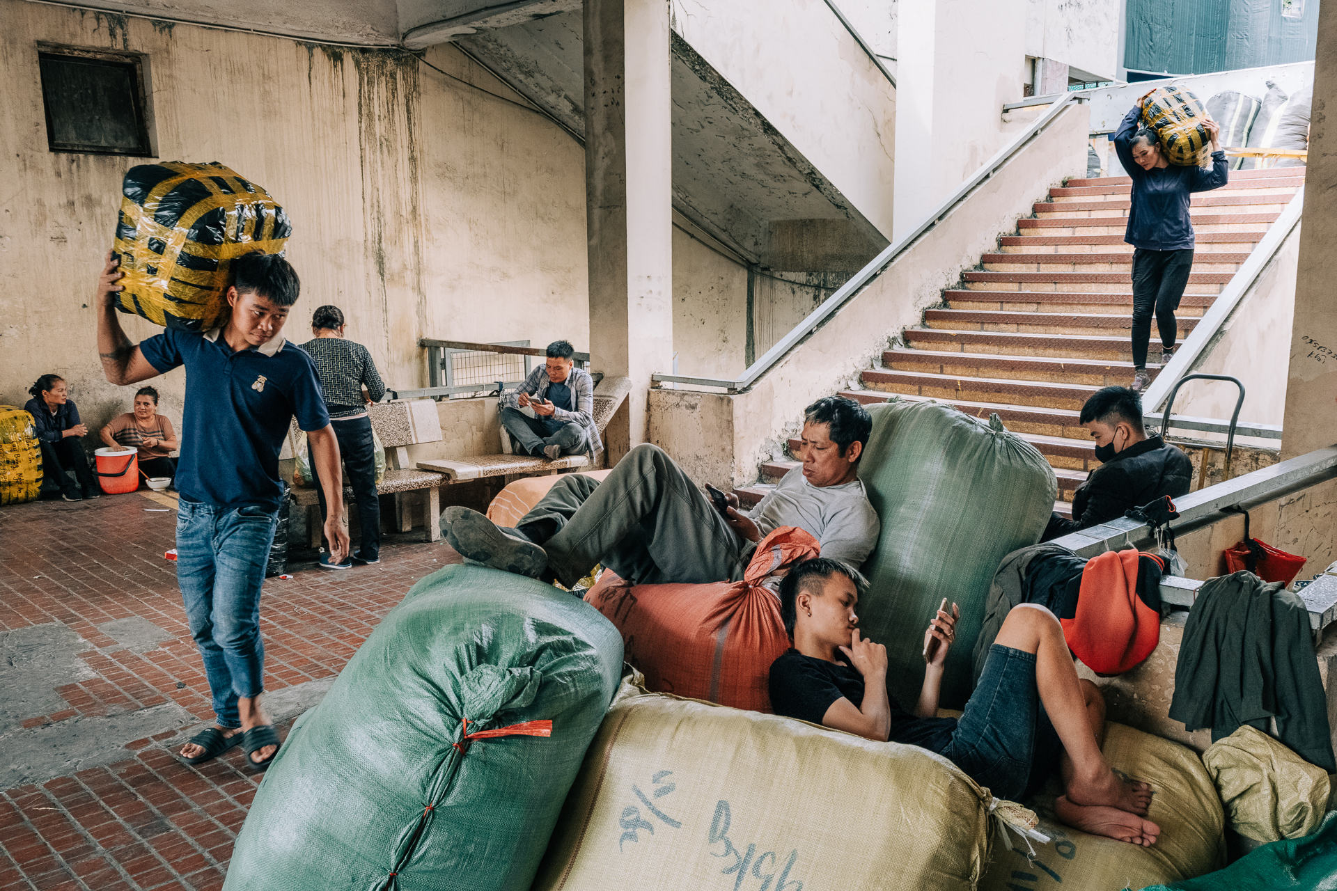 Porters and travelers resting and waiting with large sacks at Long Bien train station in Hanoi.