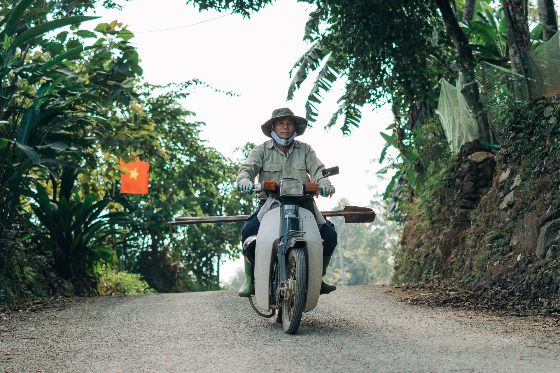Local farmer riding a motorbike on a rural road in Pu Luong, Vietnam, with Vietnamese flag in the background.